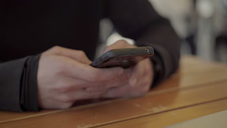 Male-hands-using-smartphone-above-wooden-table